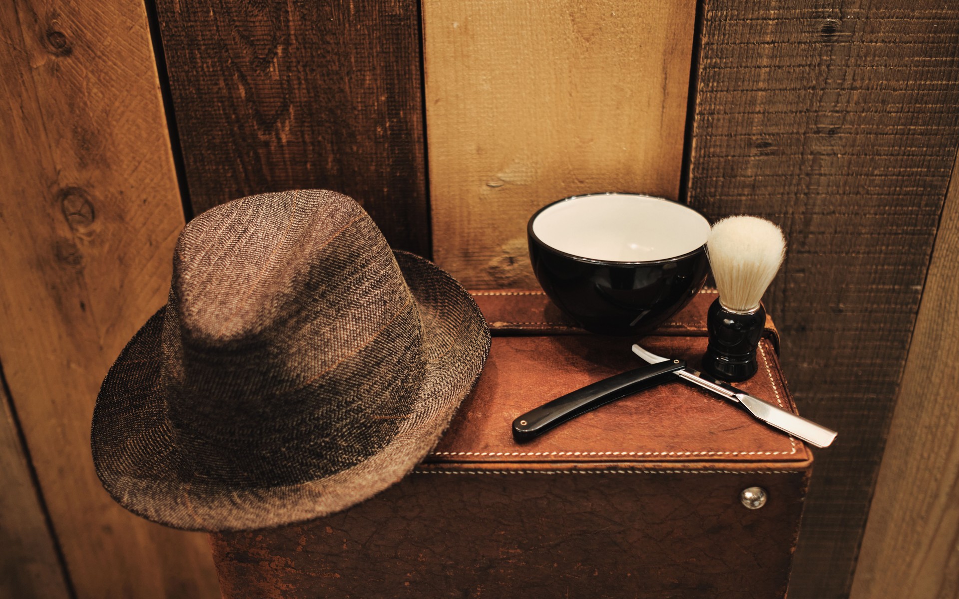 Shaving tools on an old suitcase in front of a wooden wall.